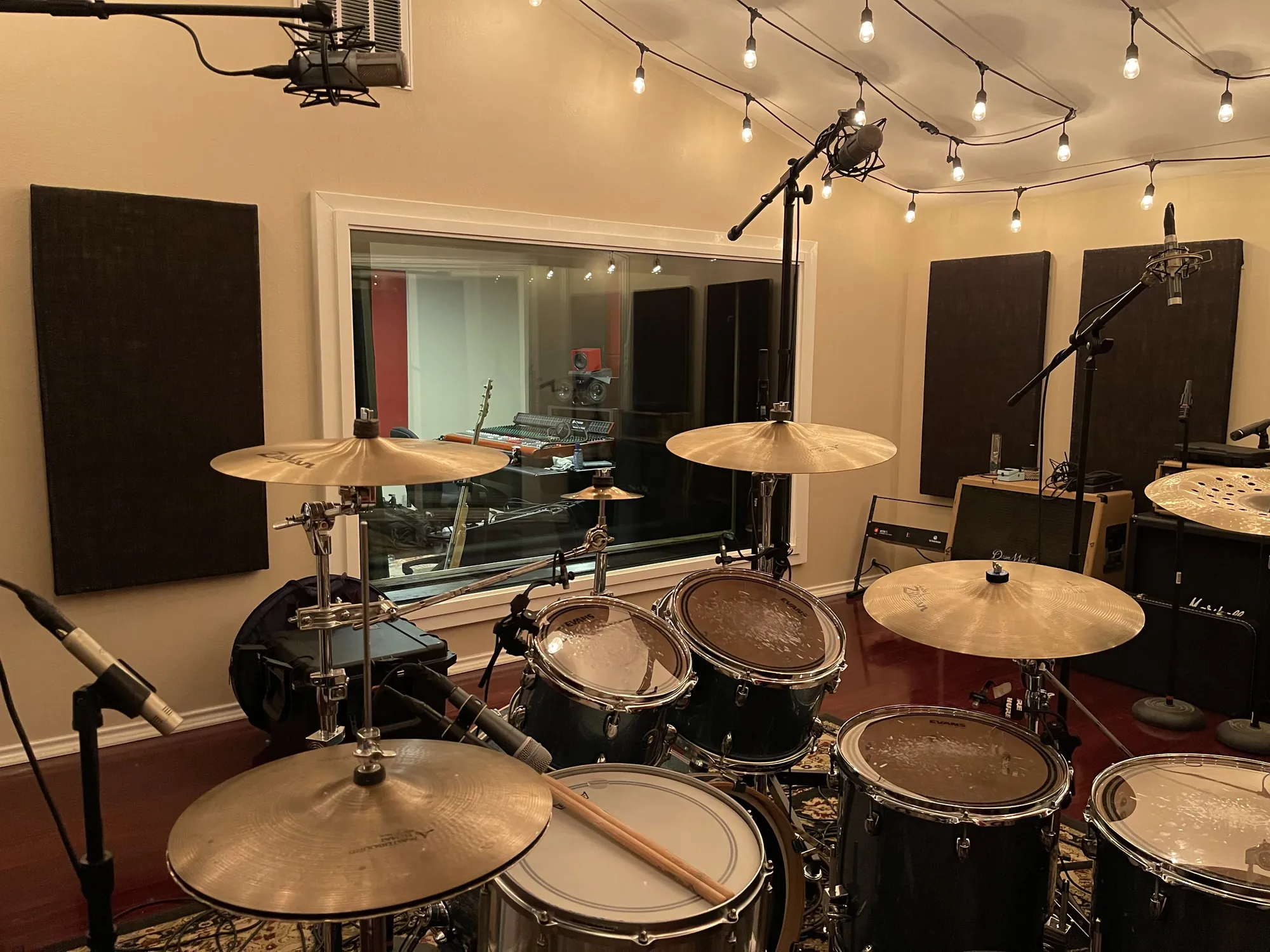 The MidWav Studio live room in New Braunfels, Texas: drum kit under string lights with the control room through the glass